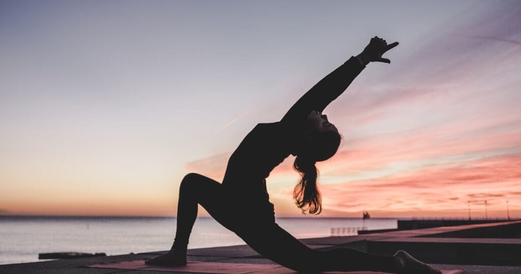 Silhouette d une personne en posture de yoga face a un coucher de soleil au bord de la mer, symbole de relaxation et de gestion du stress