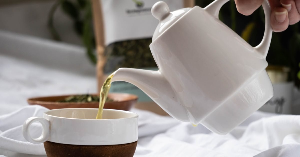 Infusion CBD versée dans une tasse, avec un bol de fleurs de chanvre séchées en arrière-plan